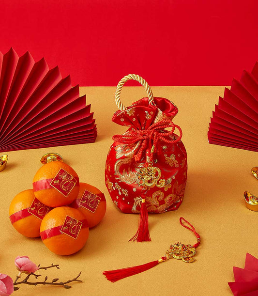 Red satin drawstring pouch with gold dragon embroidery, fresh mandarin oranges, and gold accents for Chinese New Year gifting