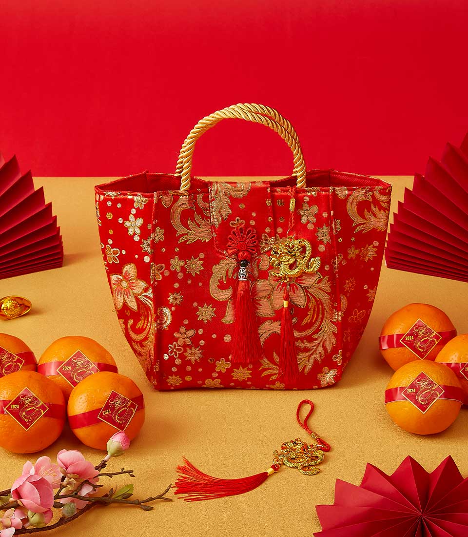 Red fabric tote with gold dragon charm filled with mandarin oranges, cherry blossoms, and Year of the Dragon accents for