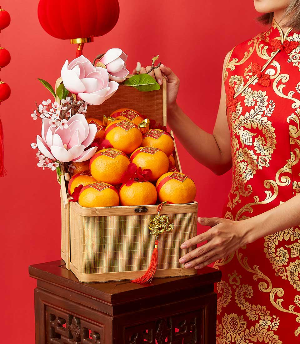 Festive CNY mandarin gift basket with pink magnolias, red ribbons, and gold dragon charm on red background