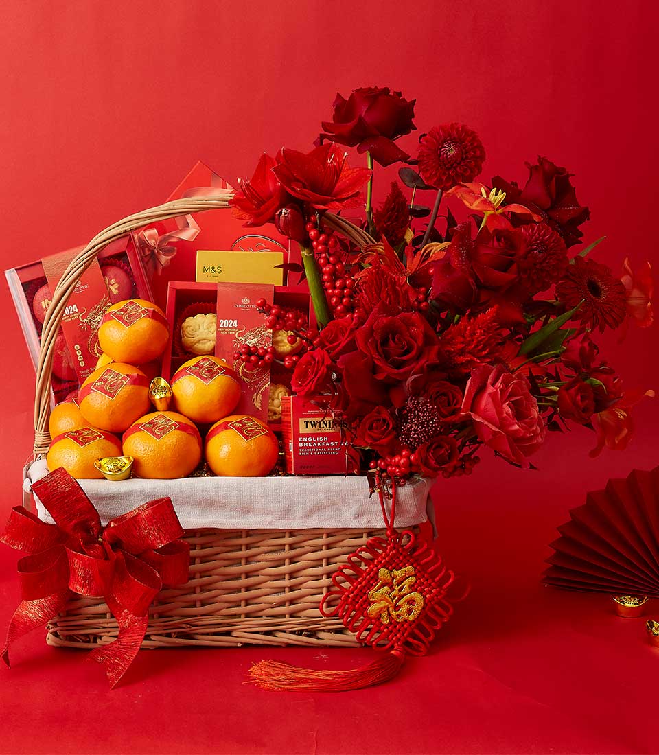 Lunar New Year wicker gift basket with mandarin oranges, red roses, premium tea, and gold prosperity charms on red background