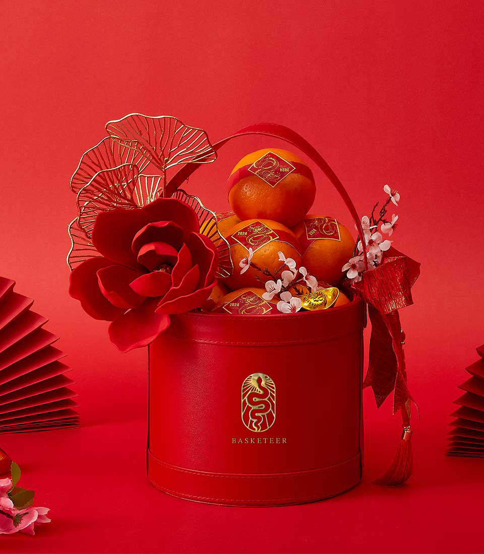 Red cylindrical gift box with mandarin oranges, dragon emblem, and traditional Chinese New Year decorations in gold and red