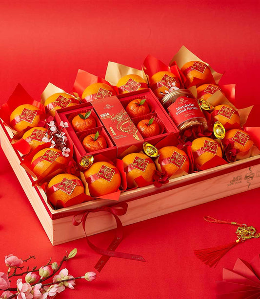 Lunar New Year gift basket with mandarin oranges, gold-wrapped treats, and lucky gold ingots on red background