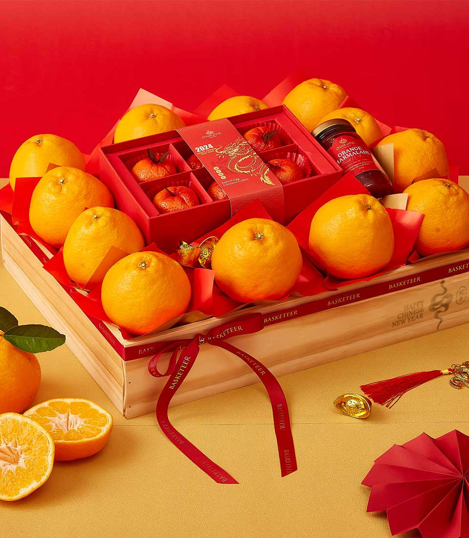 Wooden crate of fresh Dekopon oranges with red tissue, gold dragon gift box, marmalade, and festive lucky charms for Chinese