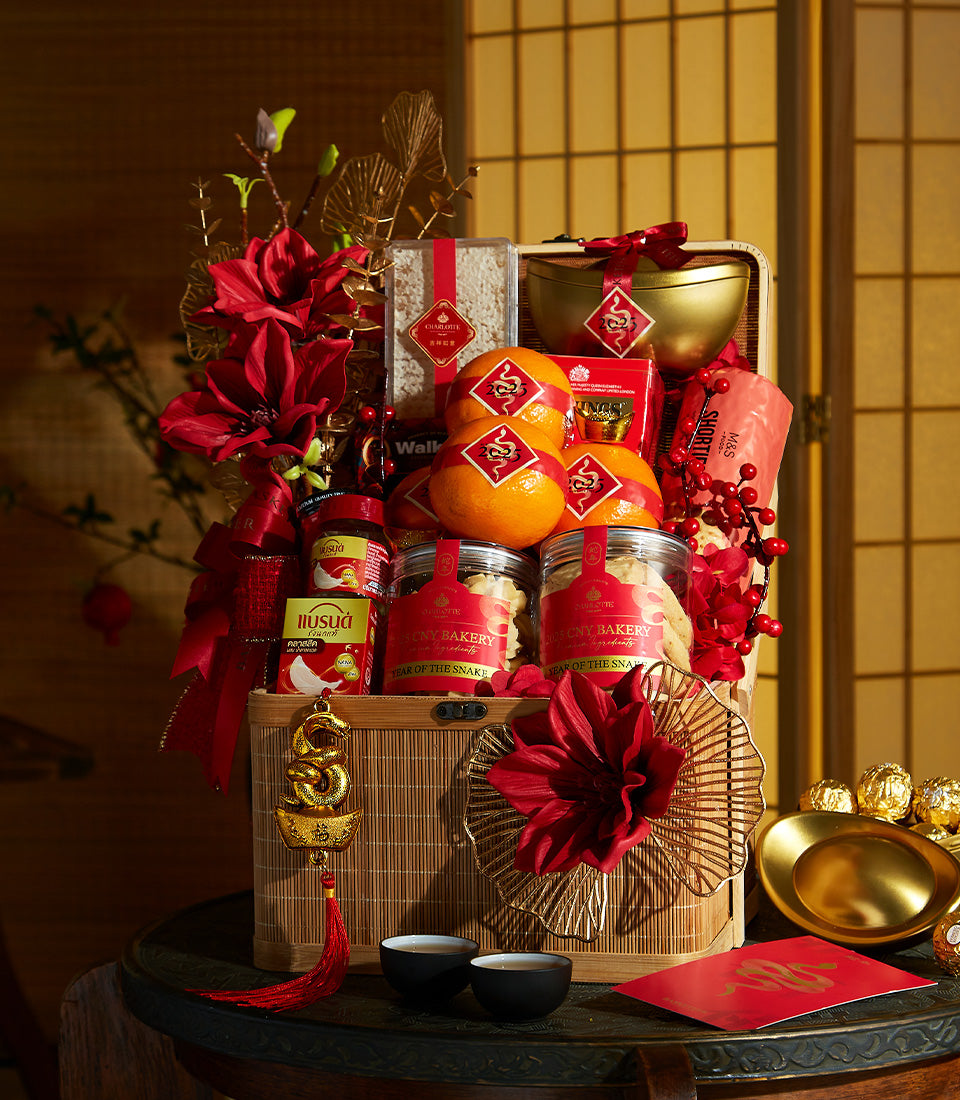 Woven bamboo prosperity hamper with red and gold Chinese New Year treats, oranges, cookies, and decorative snake charm