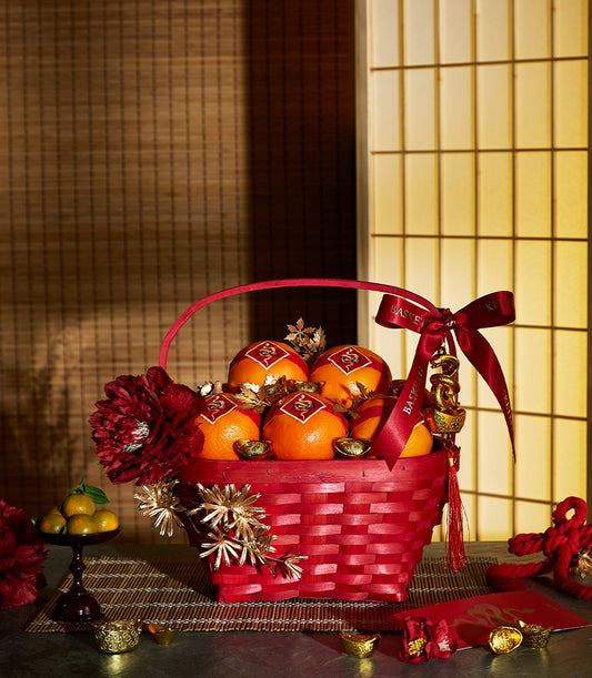Red woven basket filled with fresh oranges, gold ingots, and festive red ribbon for Chinese New Year prosperity gifting