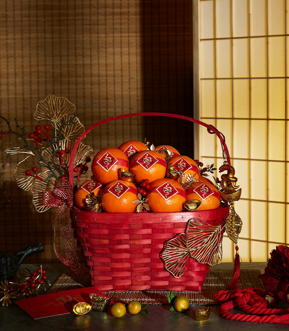 Red woven basket filled with mandarin oranges, gold snake charms, and ginkgo leaf ornaments for Chinese New Year prosperity