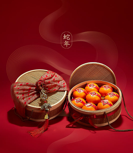 Woven bamboo gift boxes with red and gold fabric bow, silver dragon charm, and bright orange tangerines for Chinese New Year