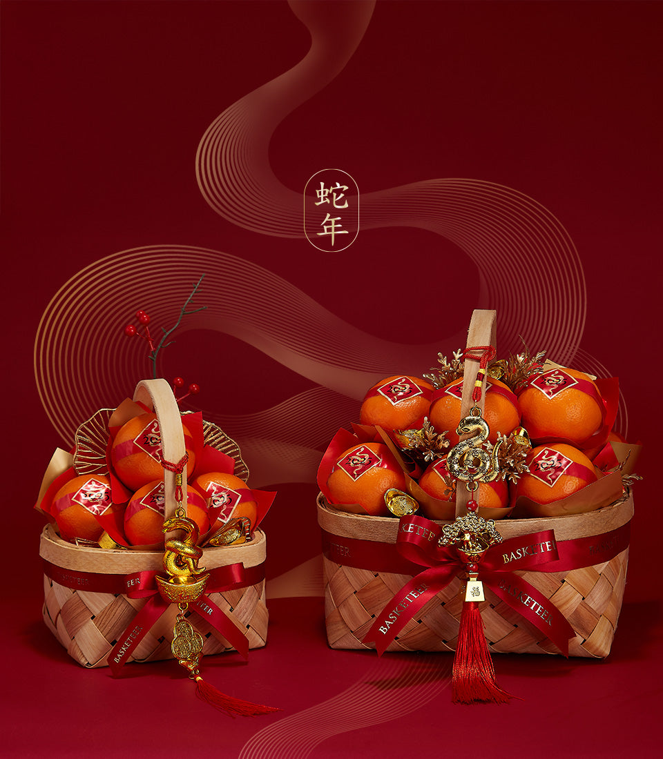 Prosperity Mandarin Gift Basket Duo with wrapped oranges, gold snake charm, and red ribbon on festive red background for