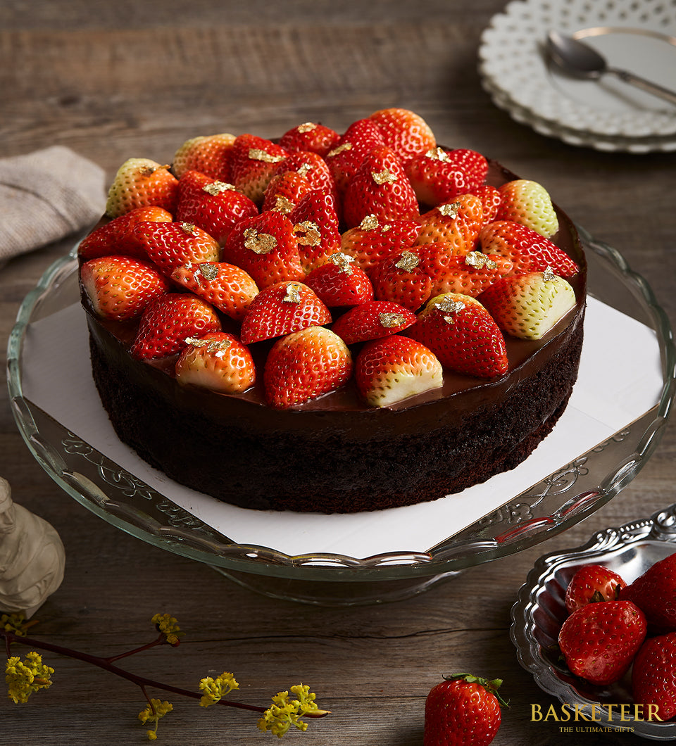 Decadent chocolate cake with fresh strawberries and gold leaf on glass cake stand