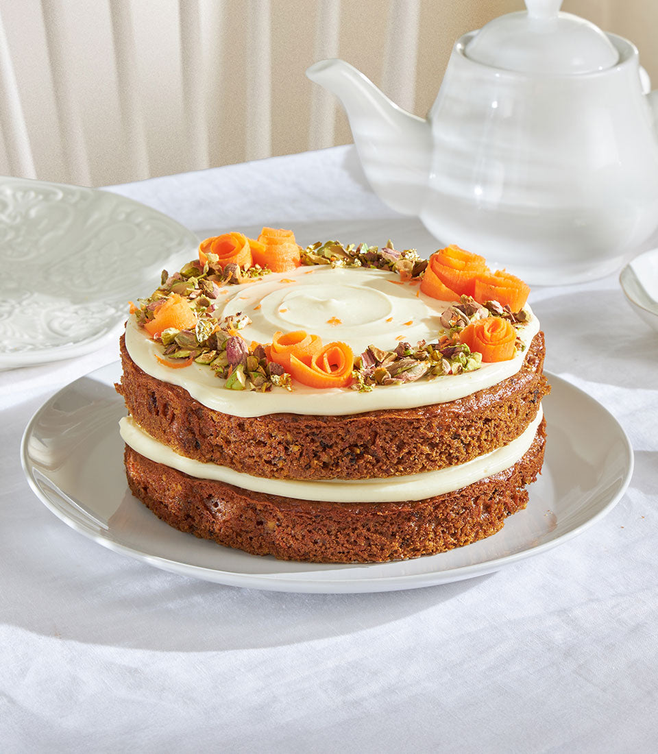 Frosted carrot sponge cake with cream cheese icing, candied carrot curls, and pistachios