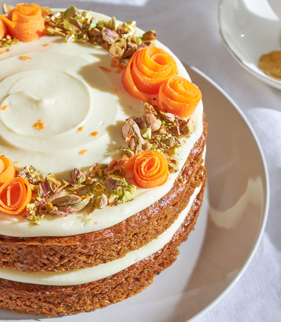 Three-tiered carrot sponge cake with cream cheese frosting, candied carrot roses, pistachios, and gold leaf