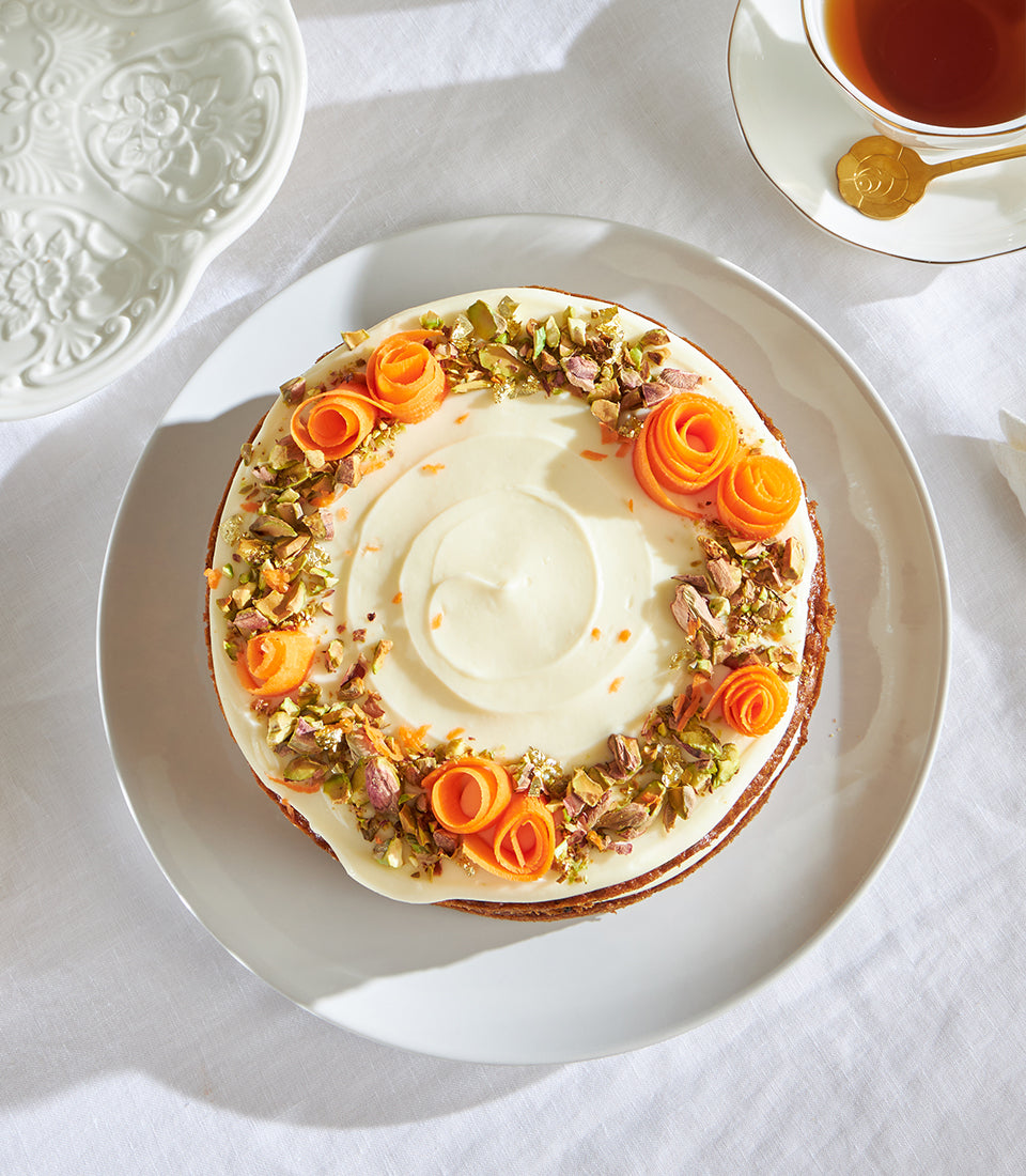 Frosted carrot birthday sponge cake with cream cheese icing, carrot curl roses and pistachio crumble
