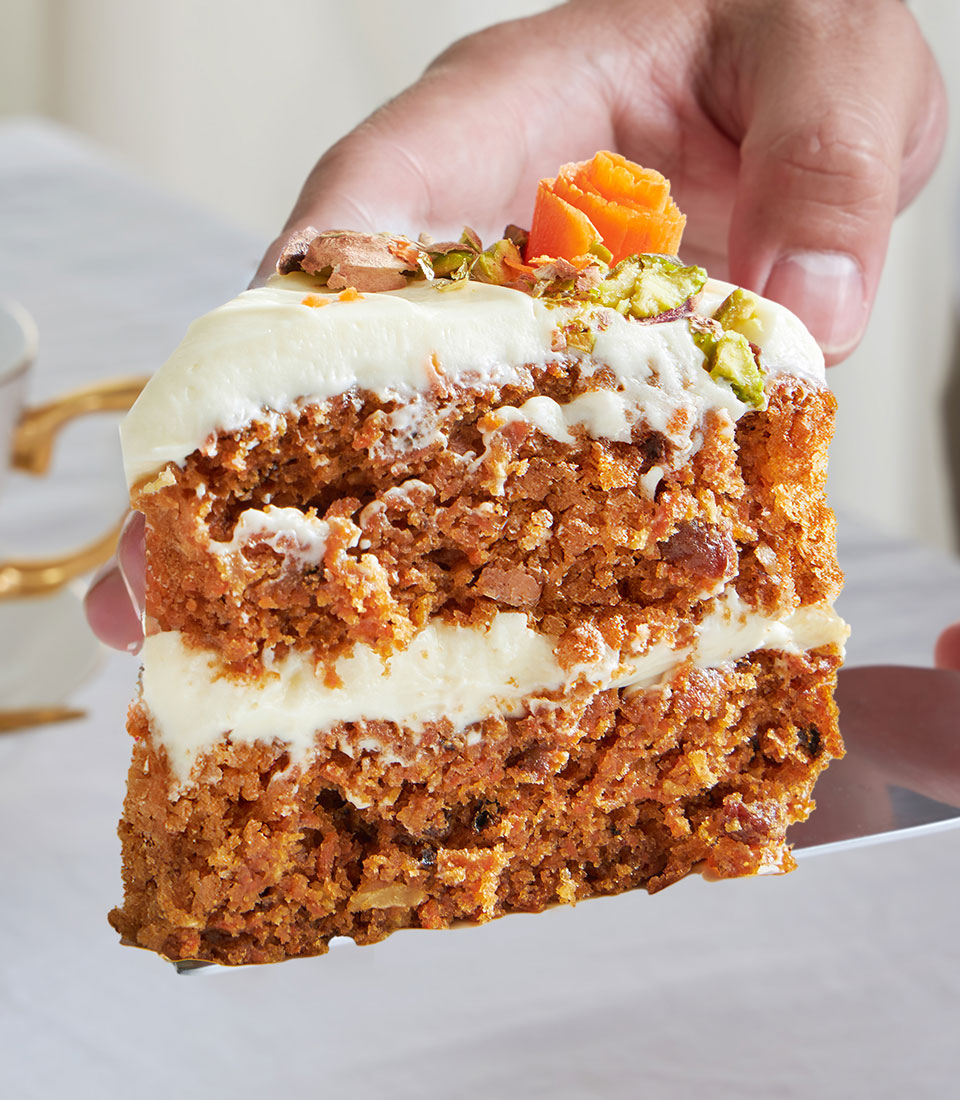 Frosted carrot cake slice with cream cheese icing, pistachios, and candied carrot garnish