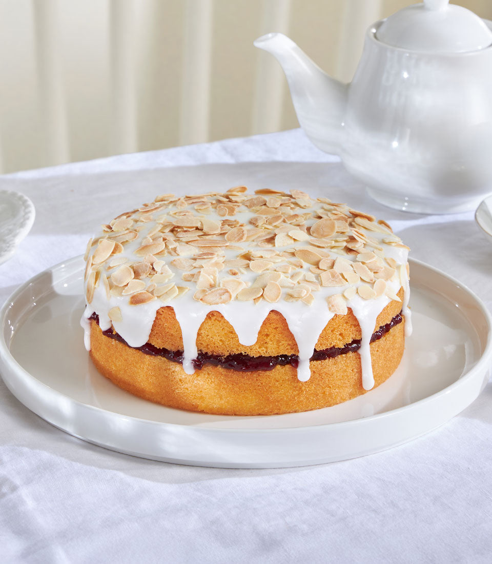 Cherry Bakewell almond cake with jam filling and white icing on rimmed plate, artisan British bakery gift
