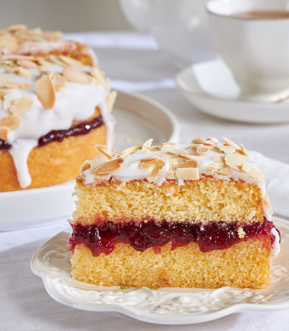 Cherry Bakewell almond cake slice with jam filling, white icing, and almond topping on decorative plate