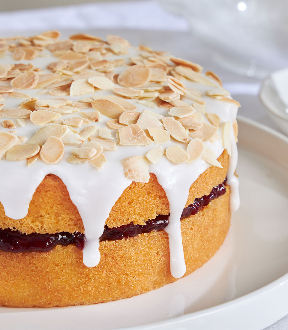 Cherry Bakewell almond birthday cake with jam filling, white icing, and toasted almond flakes