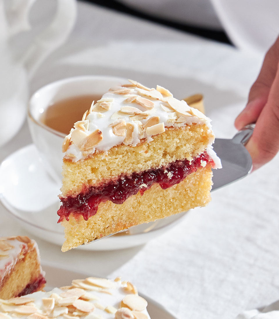 Cherry Bakewell almond cake slice with jam filling, white icing, and toasted almonds served with tea