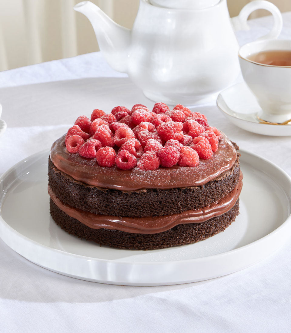 Two-layer dark chocolate cake with fresh raspberries and powdered sugar, artisan ganache filling, served on white ceramic