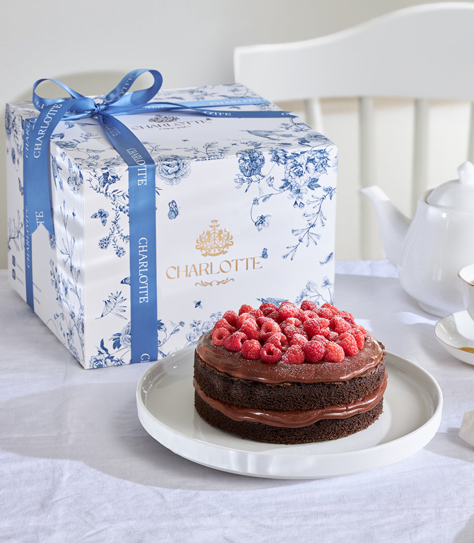 Chocolate raspberry ganache celebration cake with fresh raspberries, presented in luxury gift box with blue floral pattern