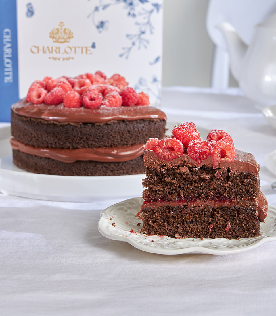 Chocolate raspberry ganache celebration cake with fresh raspberries and jam filling, plated slice and branded Charlotte