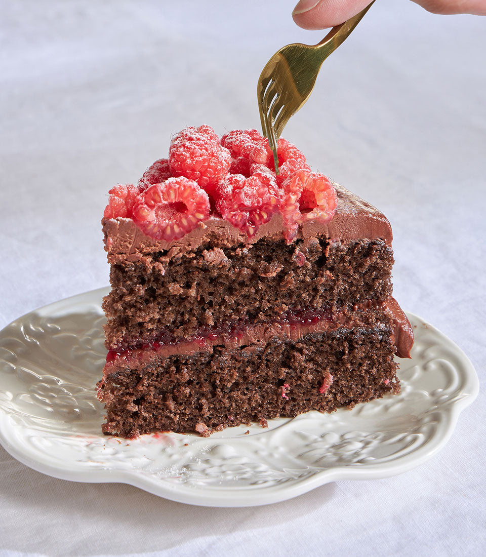 Chocolate raspberry ganache celebration cake slice with dark sponge, fresh raspberries and powdered sugar on ornate plate