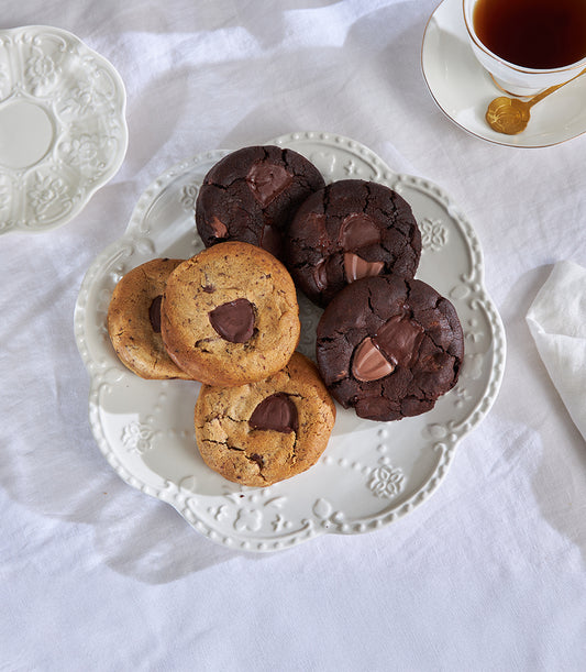 Charlotte Bakery's artisan chocolate chip cookies, classic and double chocolate, arranged on a vintage-style plate with tea. Order these baked goods in Bangkok!