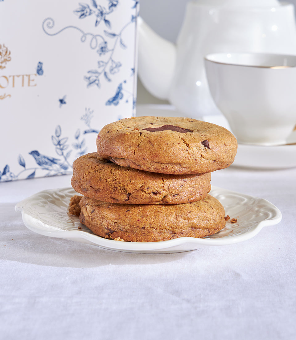 Stack of golden chocolate chip cookies on scalloped white plate, artisan bakery gift set with tea service