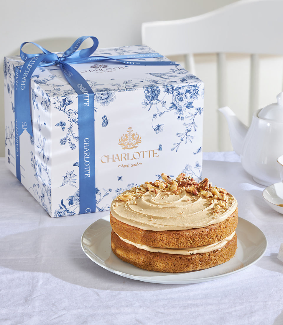 Light brown coffee and walnut layer cake with walnut frosting, presented with Charlotte Bakery gift box and blue floral