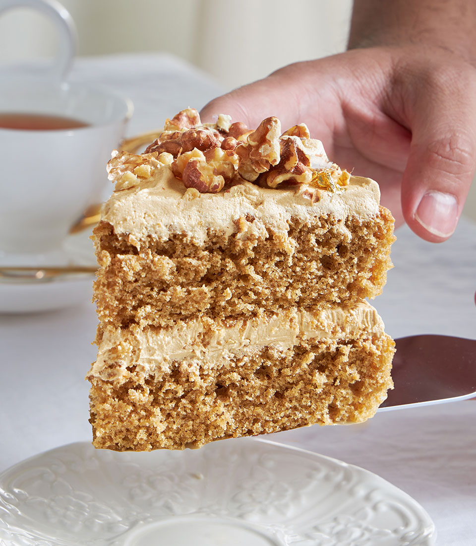 Classic coffee and walnut cake slice with creamy frosting, gold leaf, and candied walnuts on silver server