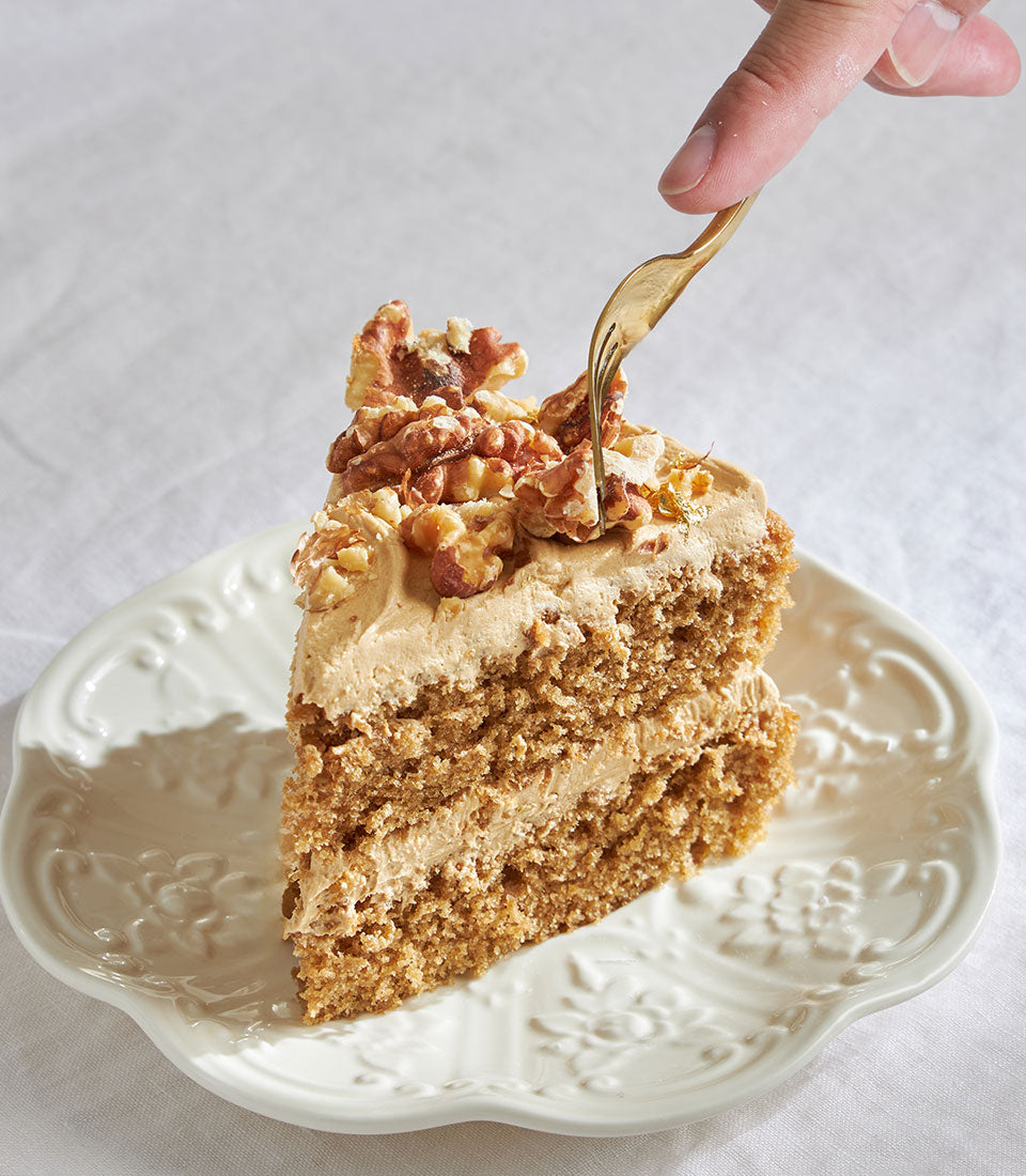 Coffee and walnut cake slice with creamy frosting and candied nuts on decorative plate