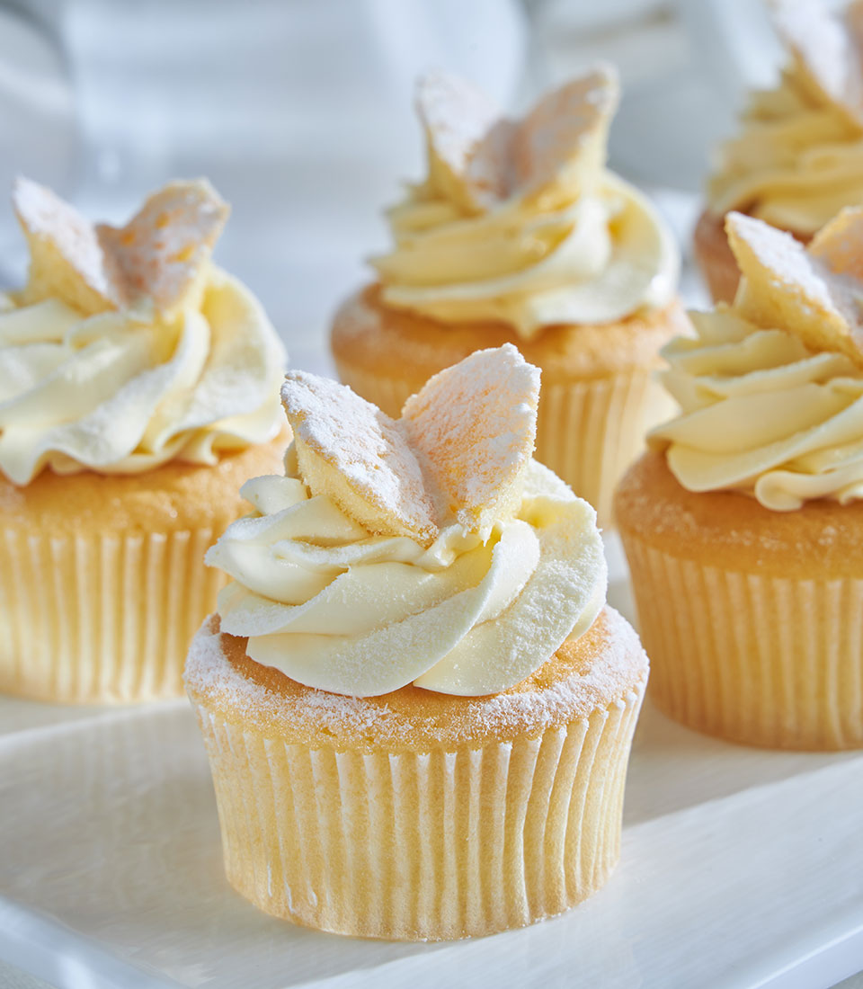 Vanilla cupcakes with white swirl frosting and butterfly cookie toppers on white tray