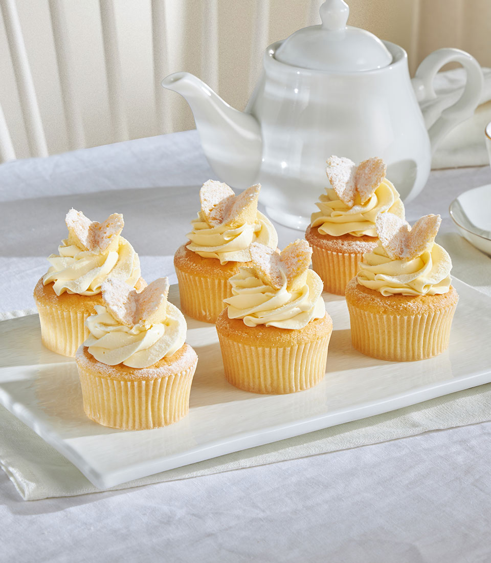 Vanilla cupcakes with light yellow frosting and butterfly meringue wafers, arranged on white platter for celebrations