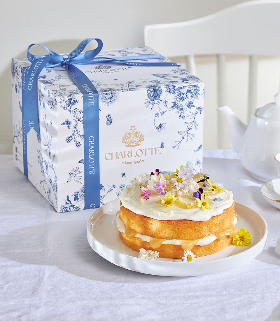 Zesty lemon drizzle cake with edible flowers in Charlotte Bakery gift box with blue floral ribbon