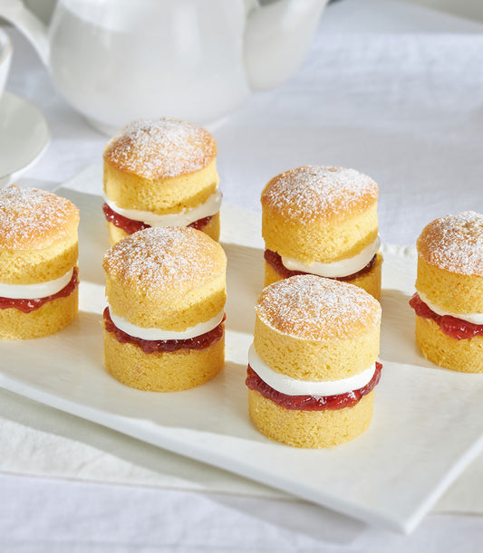 Mini Victoria sponge cakes with jam and cream filling, dusted with powdered sugar, arranged on white platter for tea parties