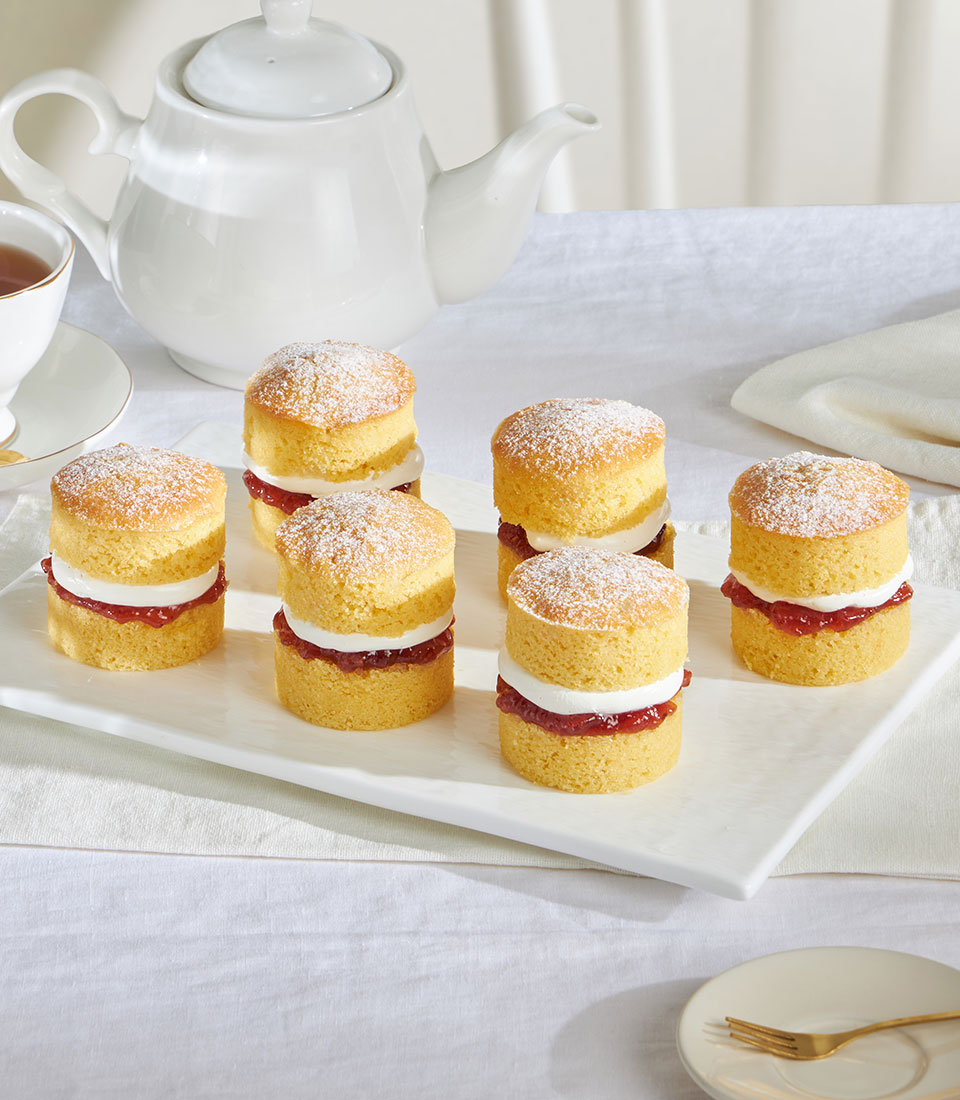 Mini Victoria sponge cakes with jam and cream filling, dusted with powdered sugar, arranged for afternoon tea