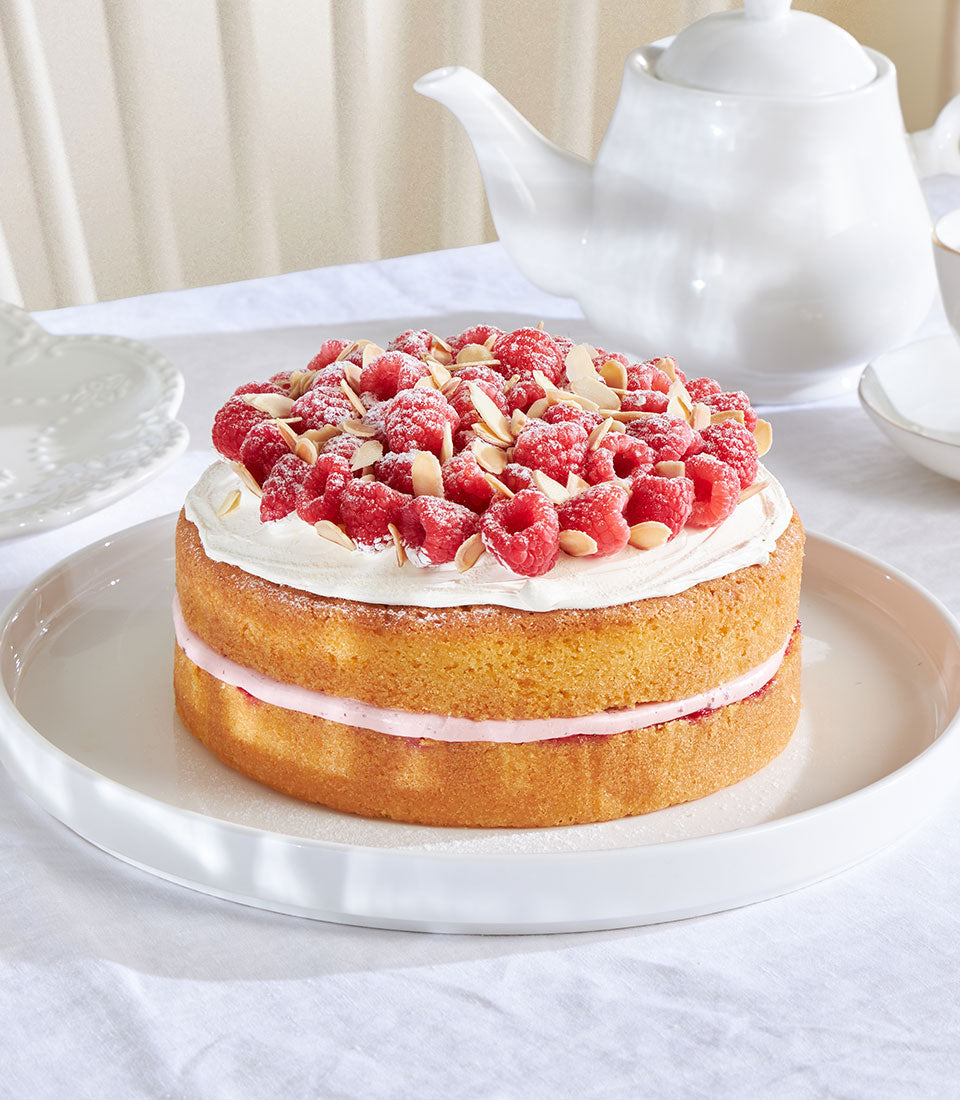 Raspberry and almond Victoria sponge cake with cream, fresh berries, and slivered almonds on white plate