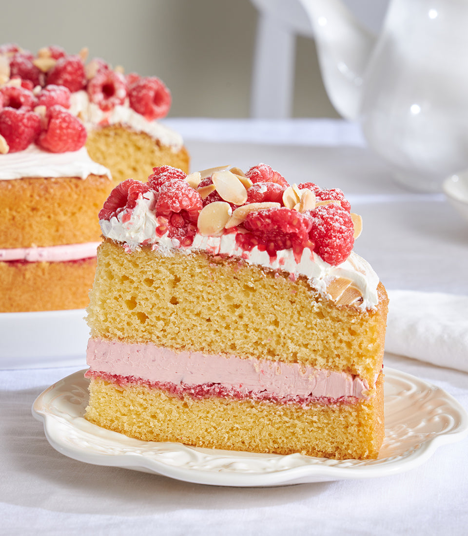 Raspberry and almond celebration cake slice with vanilla sponge, cream filling, and fresh berries