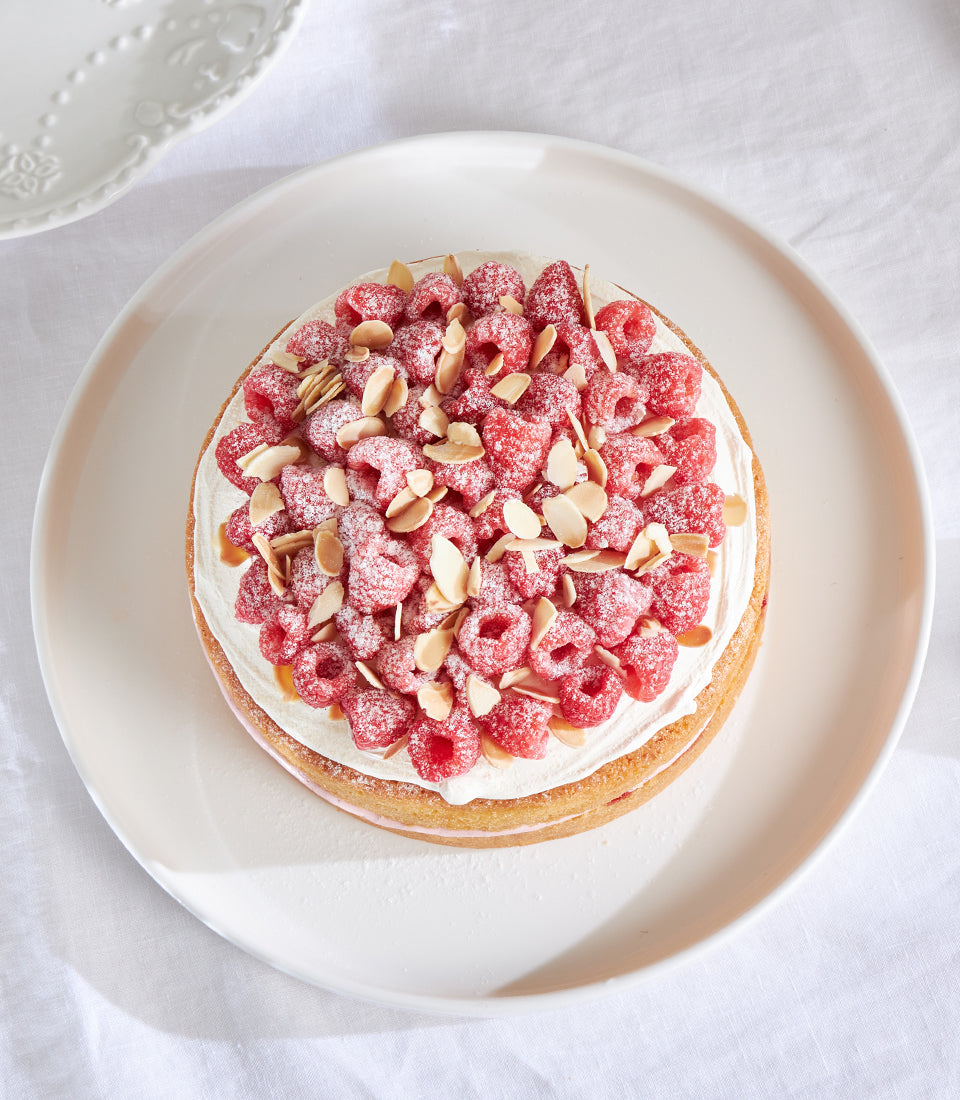 Raspberry and almond celebration cake with white cream, fresh raspberries, and toasted almonds on white serving platter
