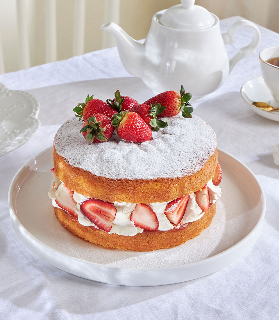 Thai-style strawberry Victoria cake with fresh berries and whipped cream on ceramic plate, tea service setting
