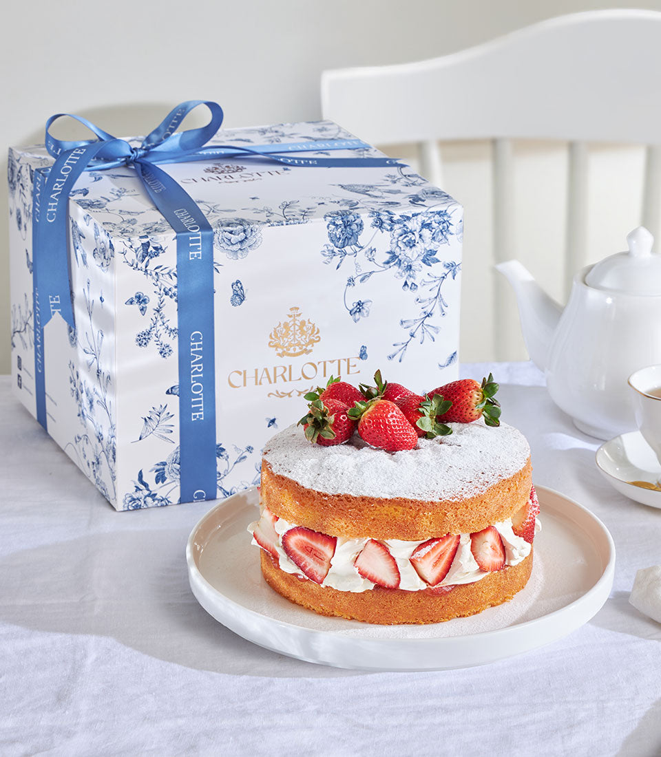 Thai-style strawberry Victoria cake with fresh berries, cream, and golden sponge layers, presented in blue floral gift box