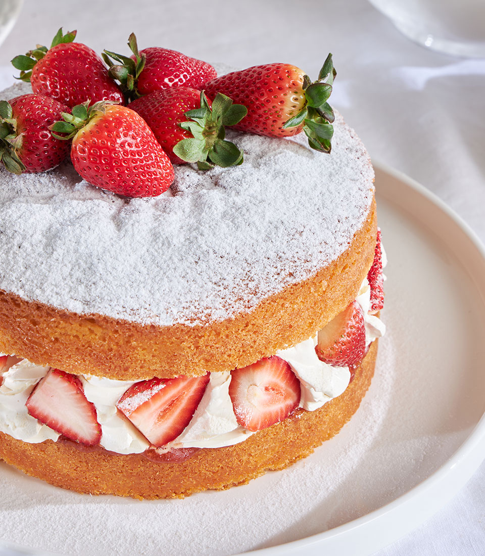 Strawberry Victoria cake with layered sponge, whipped cream, and fresh berries dusted with powdered sugar