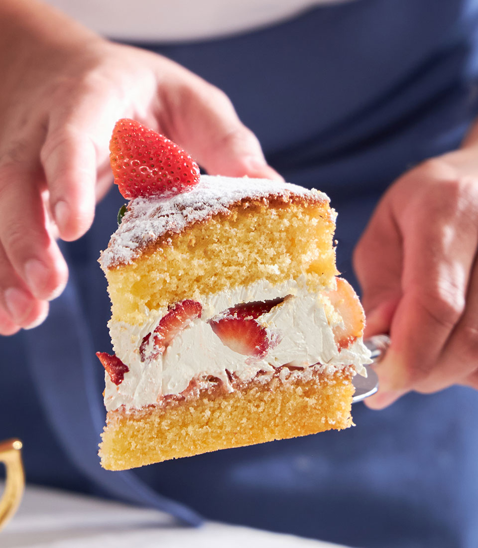 Thai-style strawberry Victoria cake slice with fresh berries, whipped cream, and golden sponge layers