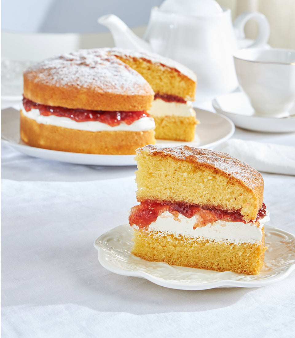Classic Victoria sponge cake with jam and cream, dusted with powdered sugar, served with tea