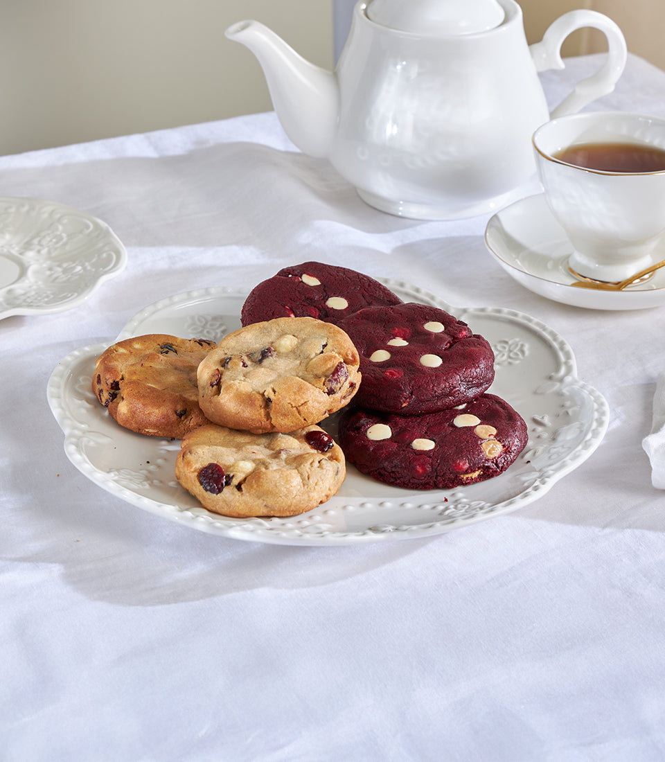 Artisan-baked cookies from Charlotte Bakery: White Choco Macadamia and Really Red Velvet, presented on a vintage plate with a pot of tea. Order custom cake Bangkok.