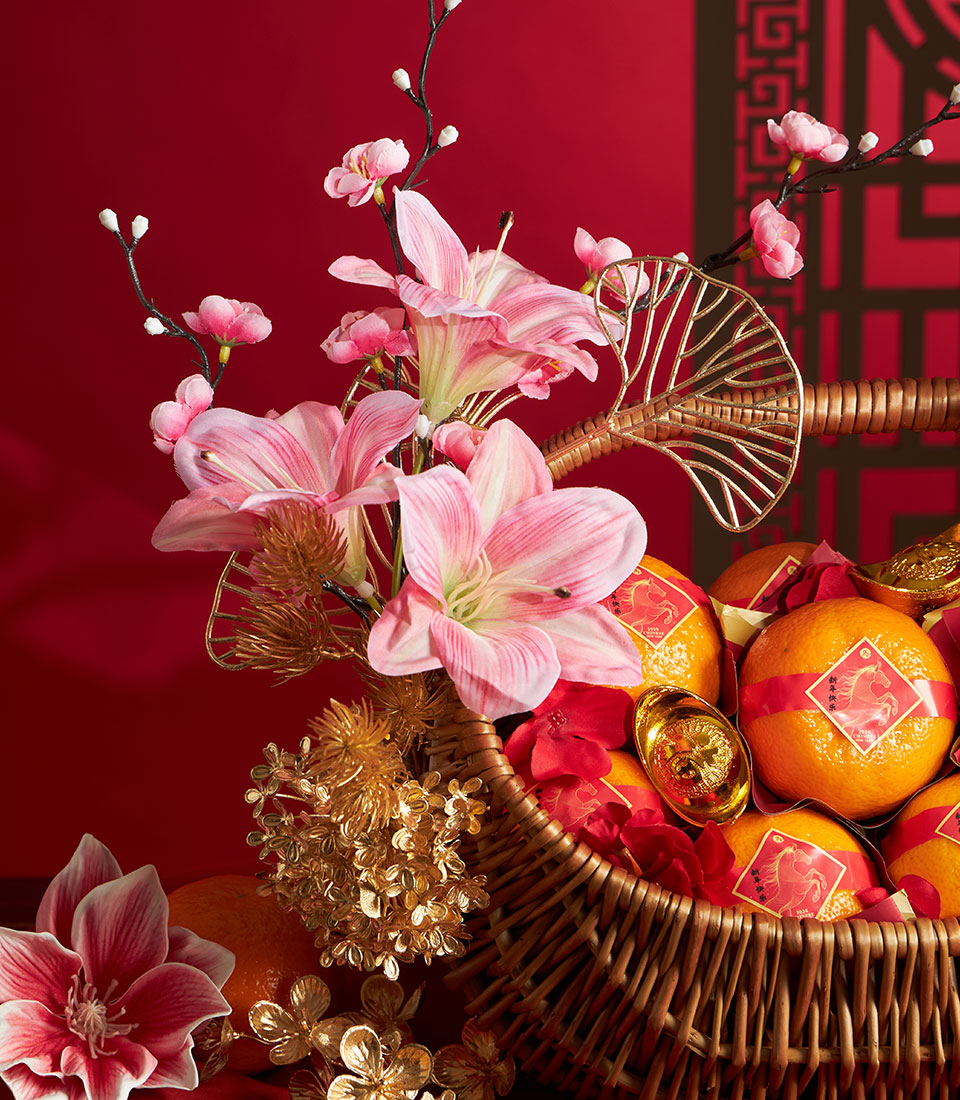 Festive Chinese New Year mandarin orange gift basket with pink lilies, gold accents, and red ribbon-wrapped fruit