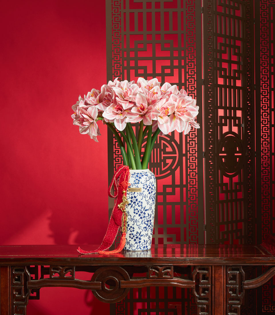 Basketeer Chinese New Year gift: Artificial amaryllis arrangement in blue and white vase with red ribbon detail. Premium floral Bangkok delivery.