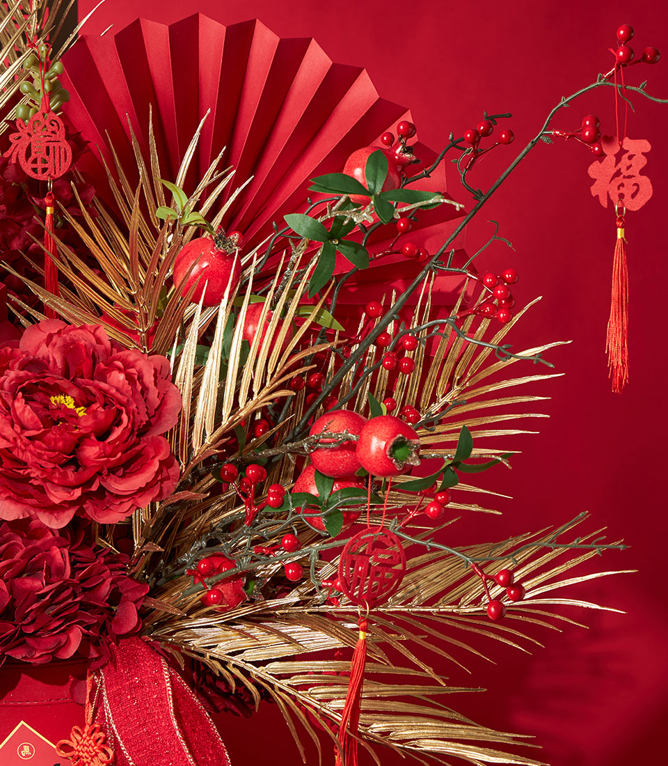 Basketeer Lunar New Year gift: red & gold floral arrangement with pomegranates, berries and golden palm fronds. Festive corporate gift for Bangkok delivery.