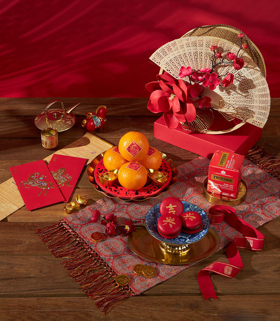 Luxury Chinese New Year gift set with mandarin oranges, English breakfast tea, and red macarons on festive red and gold