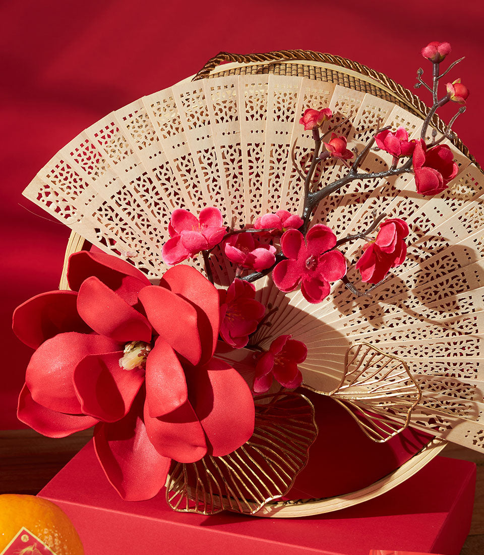 Luxury red and gold Chinese New Year gift set with carved wooden fan, fresh red flowers, and premium tea and macaron