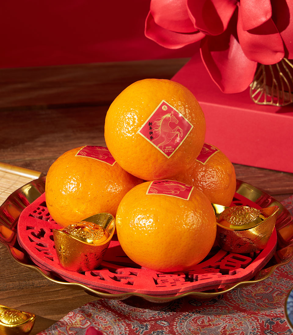 Festive mandarin oranges with Chinese New Year stickers, golden ingots, and luxury gift box with red ribbon on gold-trimmed
